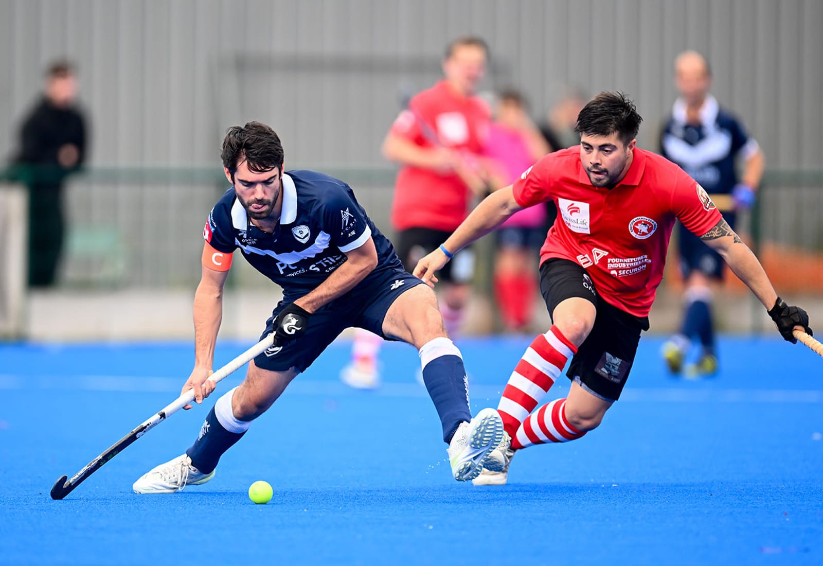 Joueur de hockey sur gazon des Girondins de Bordeaux disputant la balle à un adversaire en maillot rouge sur un terrain bleu