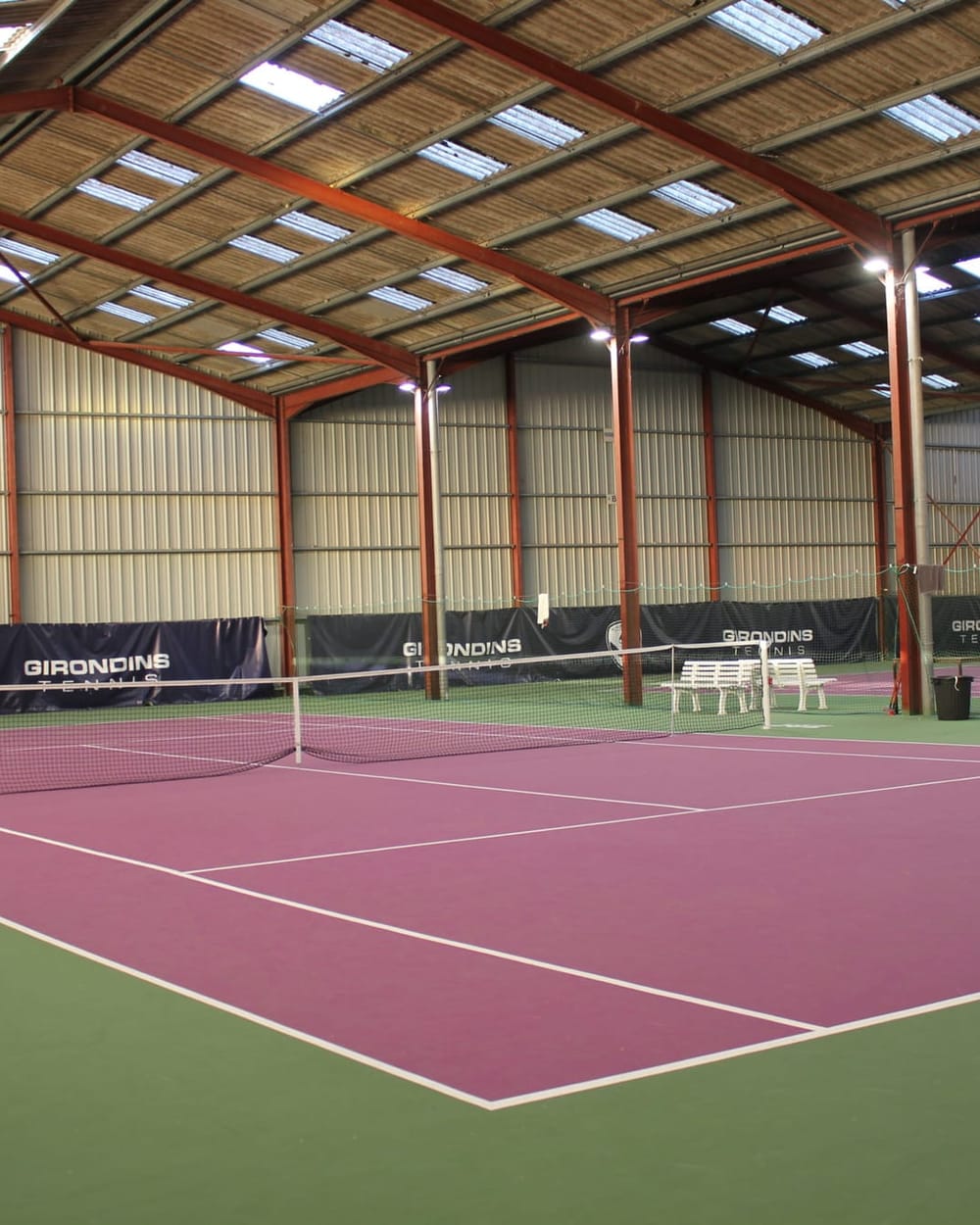 Court de tennis couvert à la surface rose, sous la charpente du Domaine de Rocquevielle